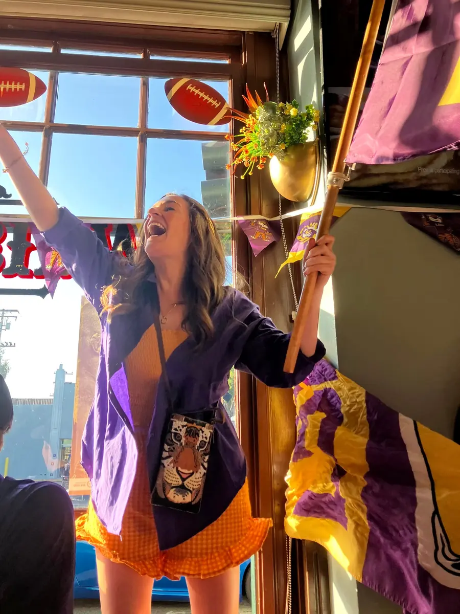 An LSU fan cheering with a purple and gold flag on game day